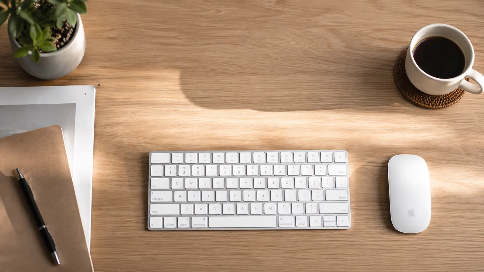 Clean home office desk with a wireless keyboard and mouse on a white surface, morning light from a window to the left